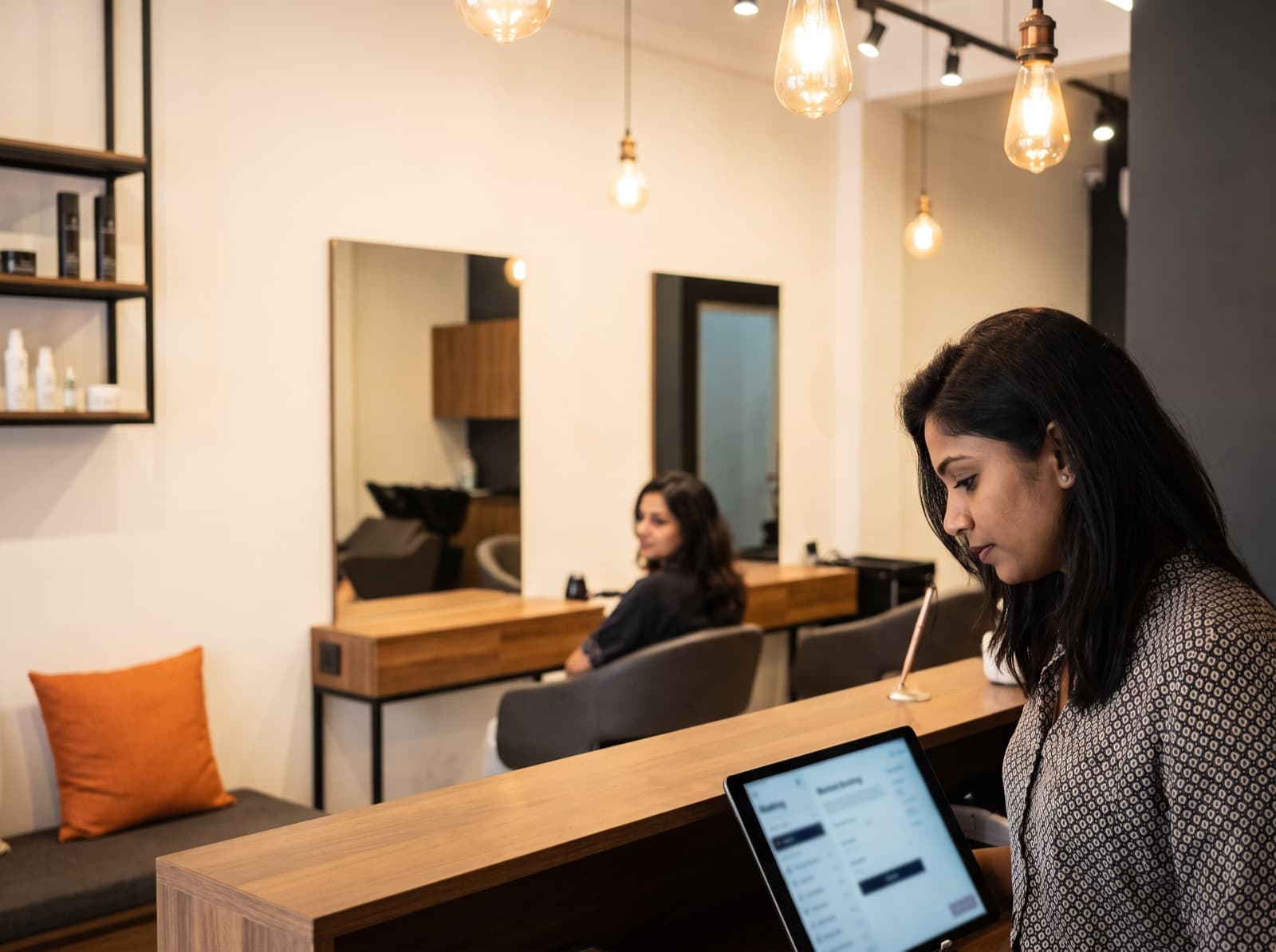 A stylist checking the booking screen at a salon front desk.